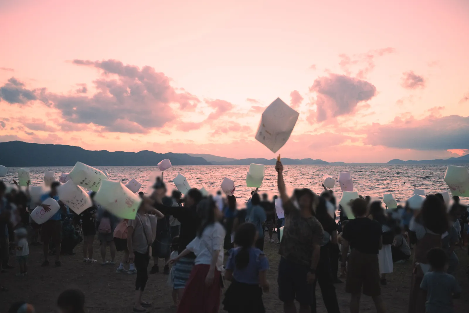 湖南 湖まつりの湖畔で灯籠を掲げる参加者と夕焼けの猪苗代湖