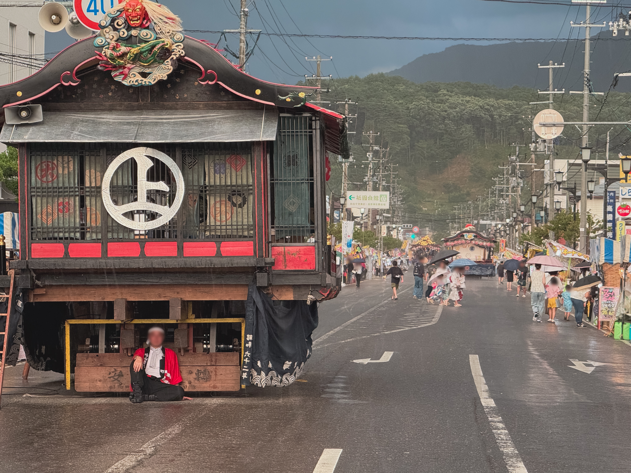 雨の中、大屋台の下で雨宿りする人（会津田島祇園祭）